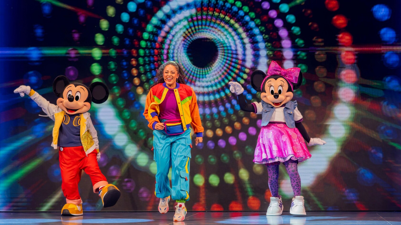 Mickey Mouse and Minnie Mouse, wearing DJ outfits, are joined by a friend on stage