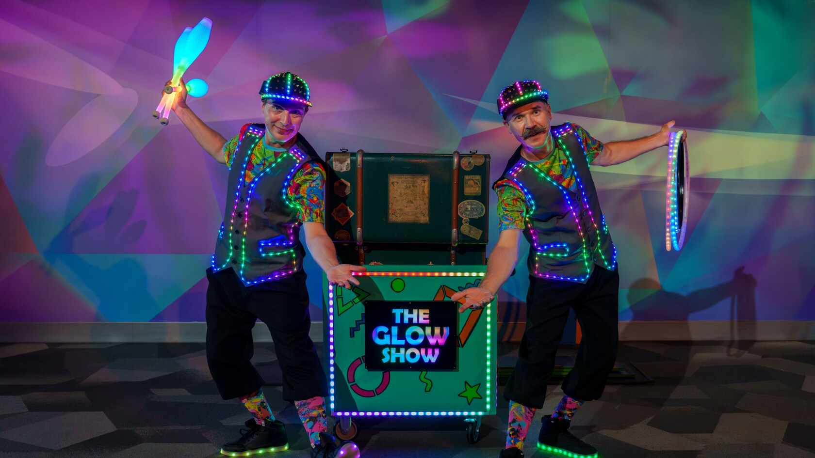 Max & Aydar, performers with glowing props next to a cart with a sign that reads, ‘The Glow Show’