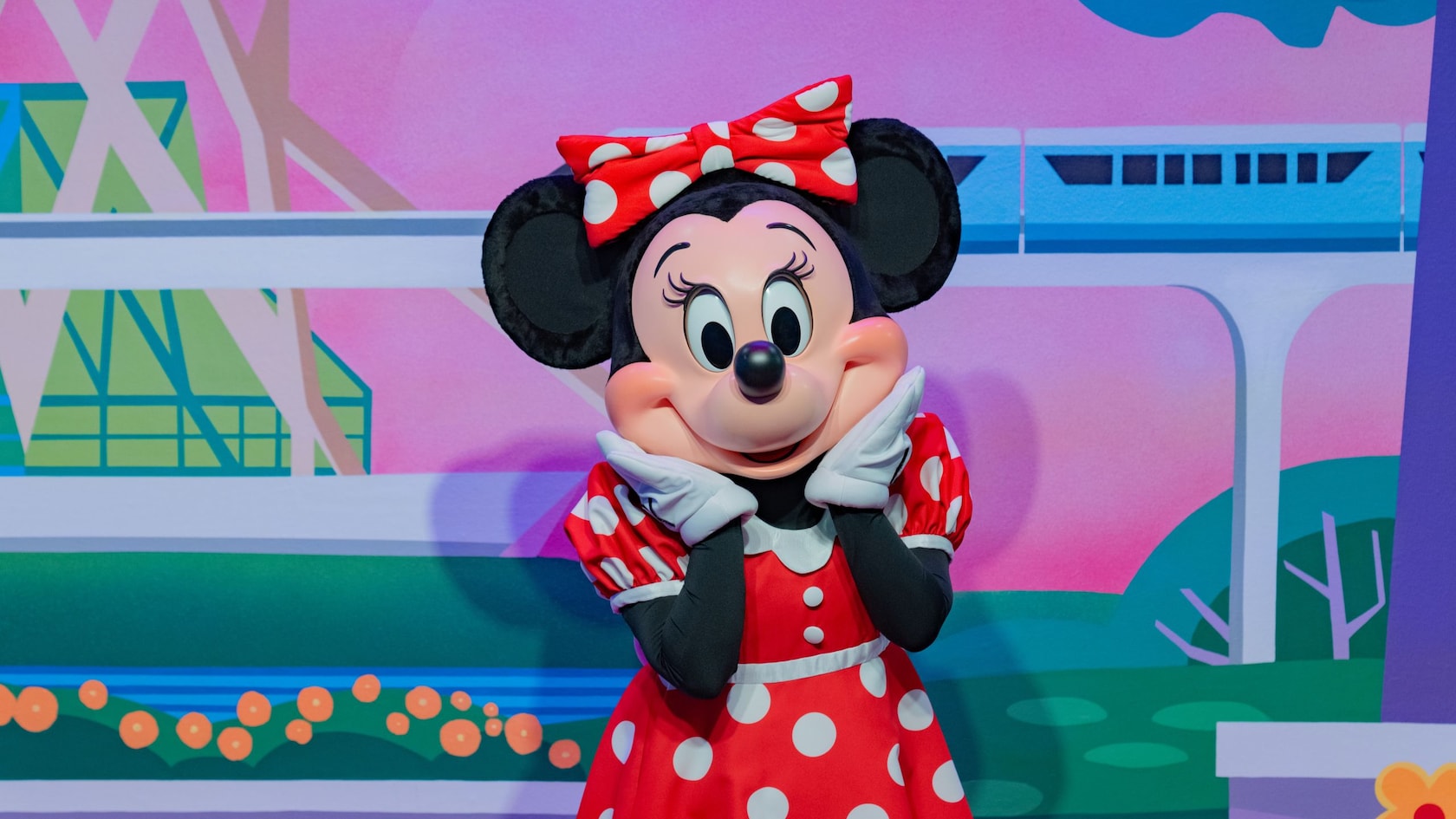 Minnie Mouse posing in front of a backdrop of a monorail traveling through Epcot