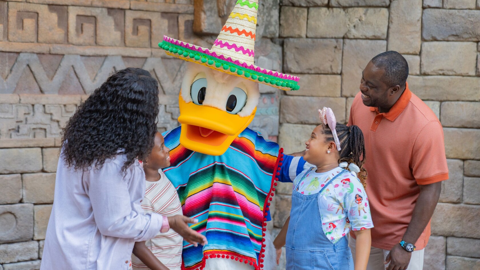 A family of 4 greeting Donald Duck wearing a poncho and sombrero