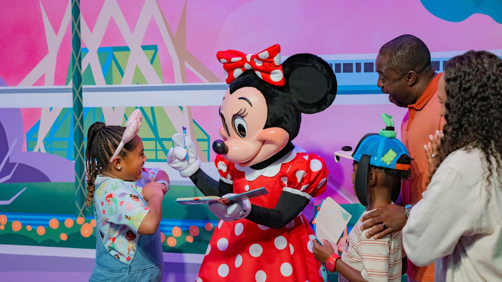 Minnie Mouse signing the autograph books of 2 children as their parents watch