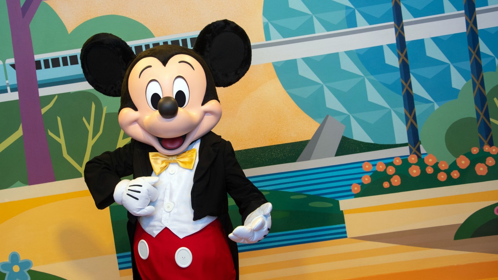 Mickey Mouse posing in front of a backdrop of a monorail traveling through Epcot