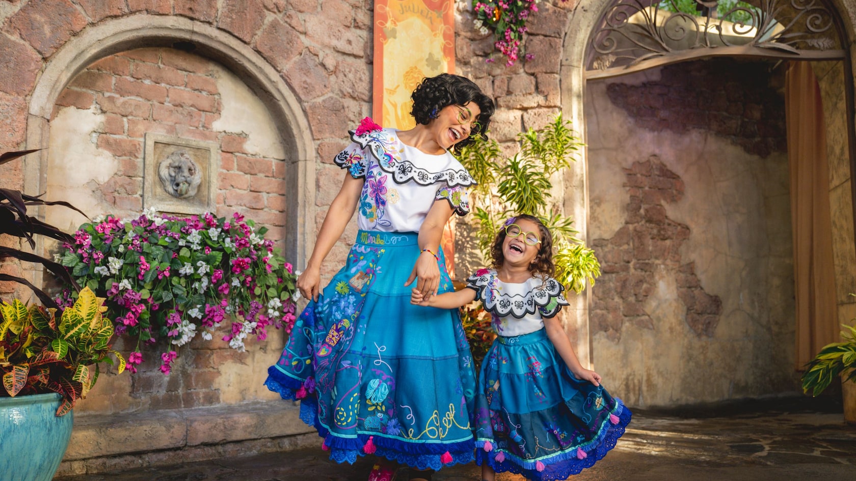 Una niña pequeña vestida como Mirabel Madrigal se toma de las manos con Mirabel Madrigal en Fairytale Garden