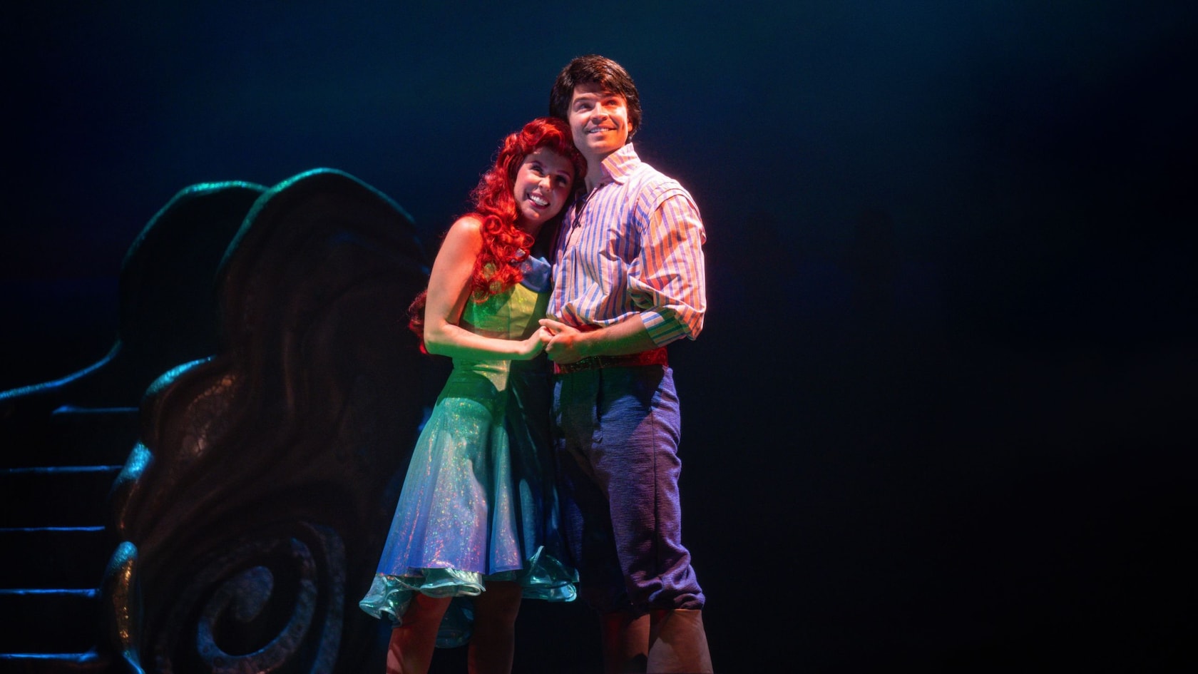 Princess Ariel and Prince Eric stand in front of a giant sea shell, holding hands