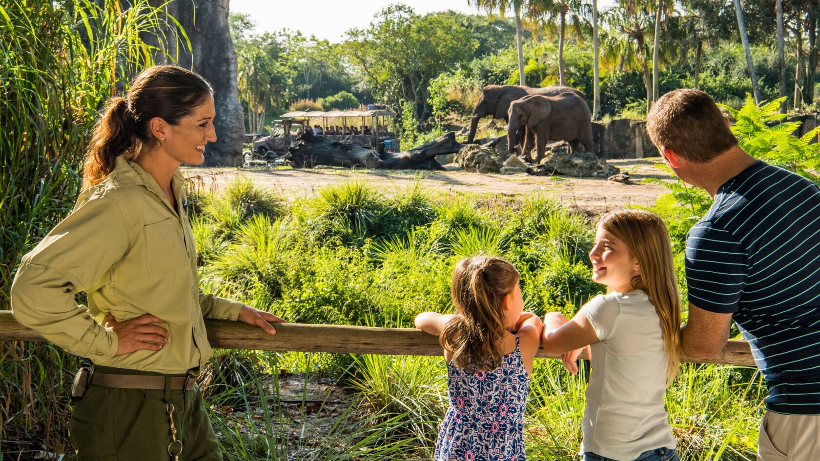 A guide and a family watching 2 elephants near a tram carrying guests at Harambe Wildlife Preserve  