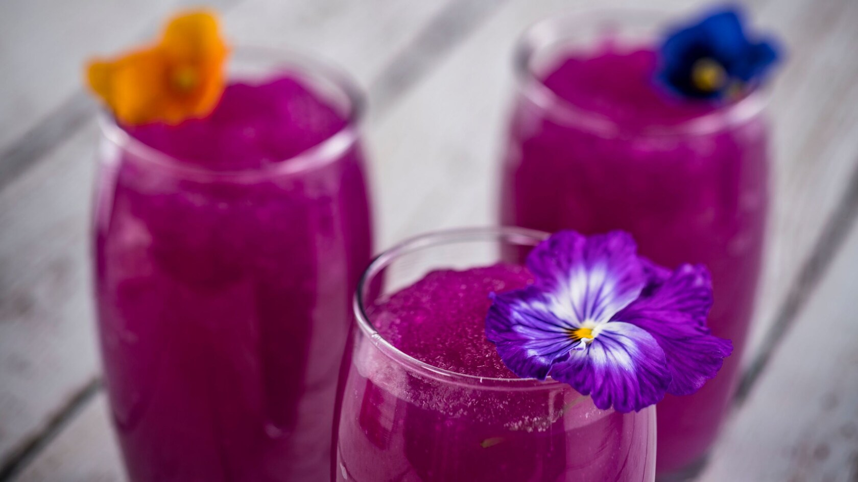 Three glasses of Frozen Desert Violet Lemonade garnished with edible flowers