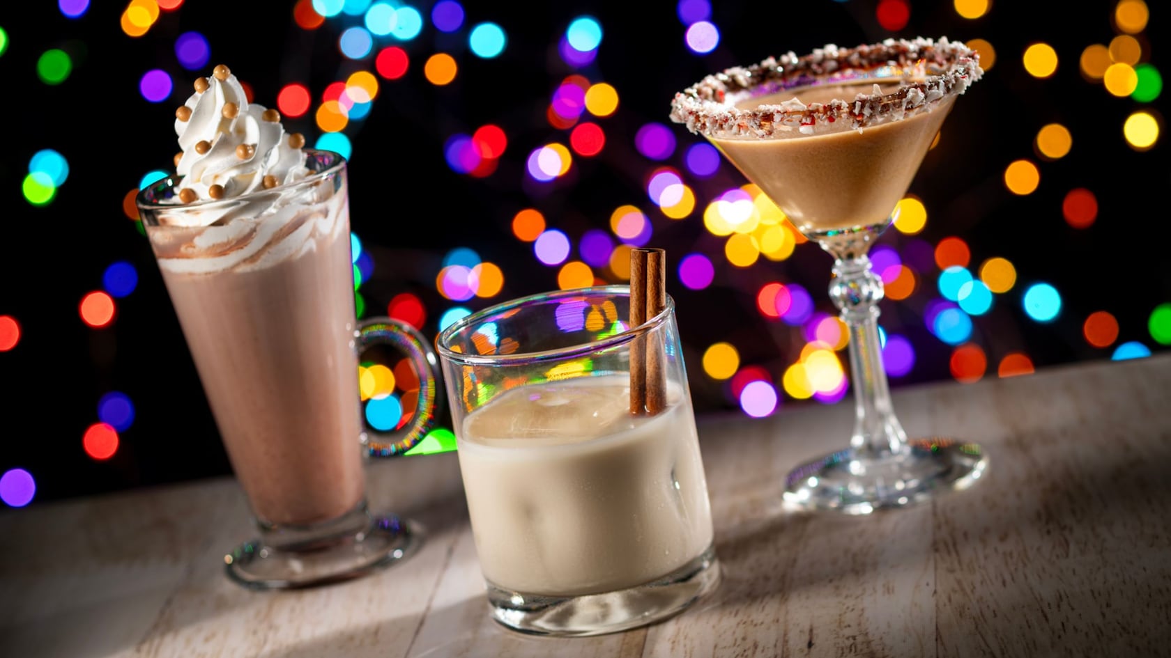 Three beverages including a whipped cream topped hot chocolate, a creamy cocktail and a cinnamon garnished drink