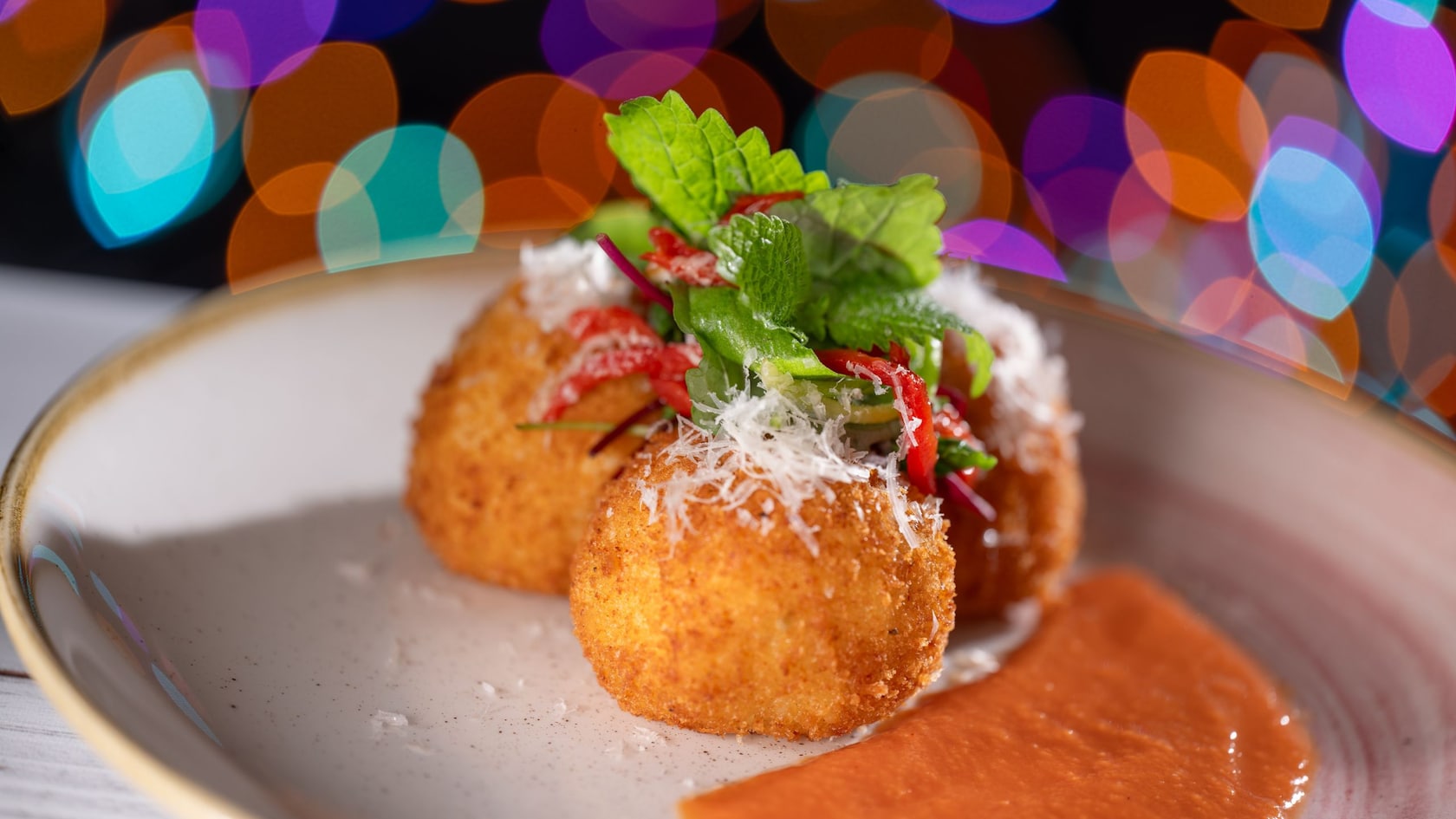 A plate of chorizo arancini topped with shredded cheese, peppers and fresh herbs, served with dipping sauce