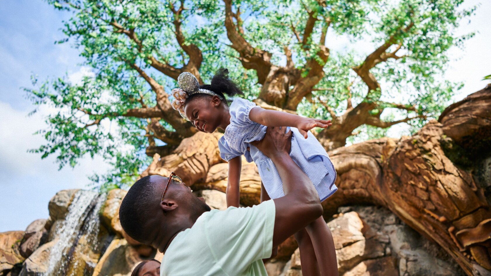 A dad lifts his daughter in the air near the Tree of Life