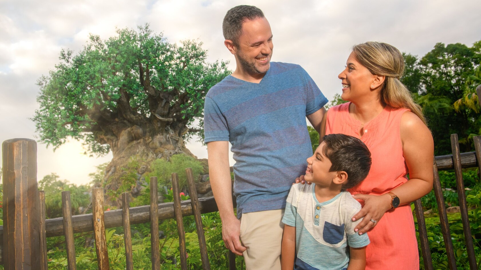 In front of a fence by the Tree of Life in Disney’s Animal Kingdom park, a delighted father and mother exchange smiles as their happy son looks on