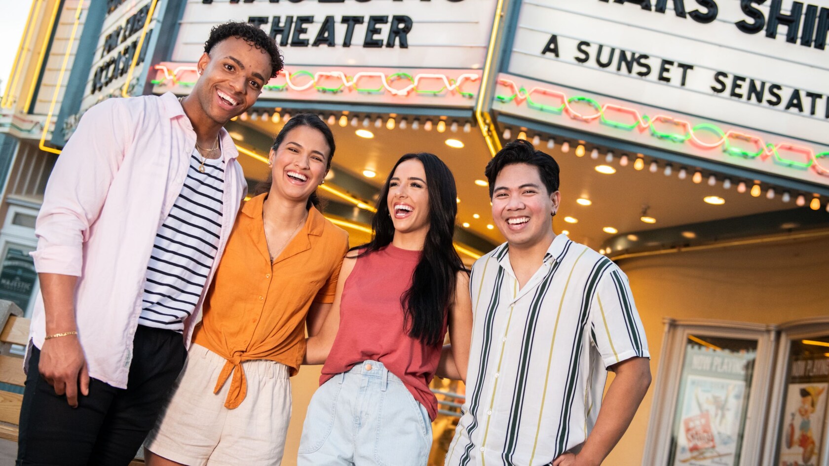 Deux jeunes couples sourient tous en se tenant debout devant l’entrée du Majestic Theater à Disney Hollywood Studios au Walt Disney World Resort