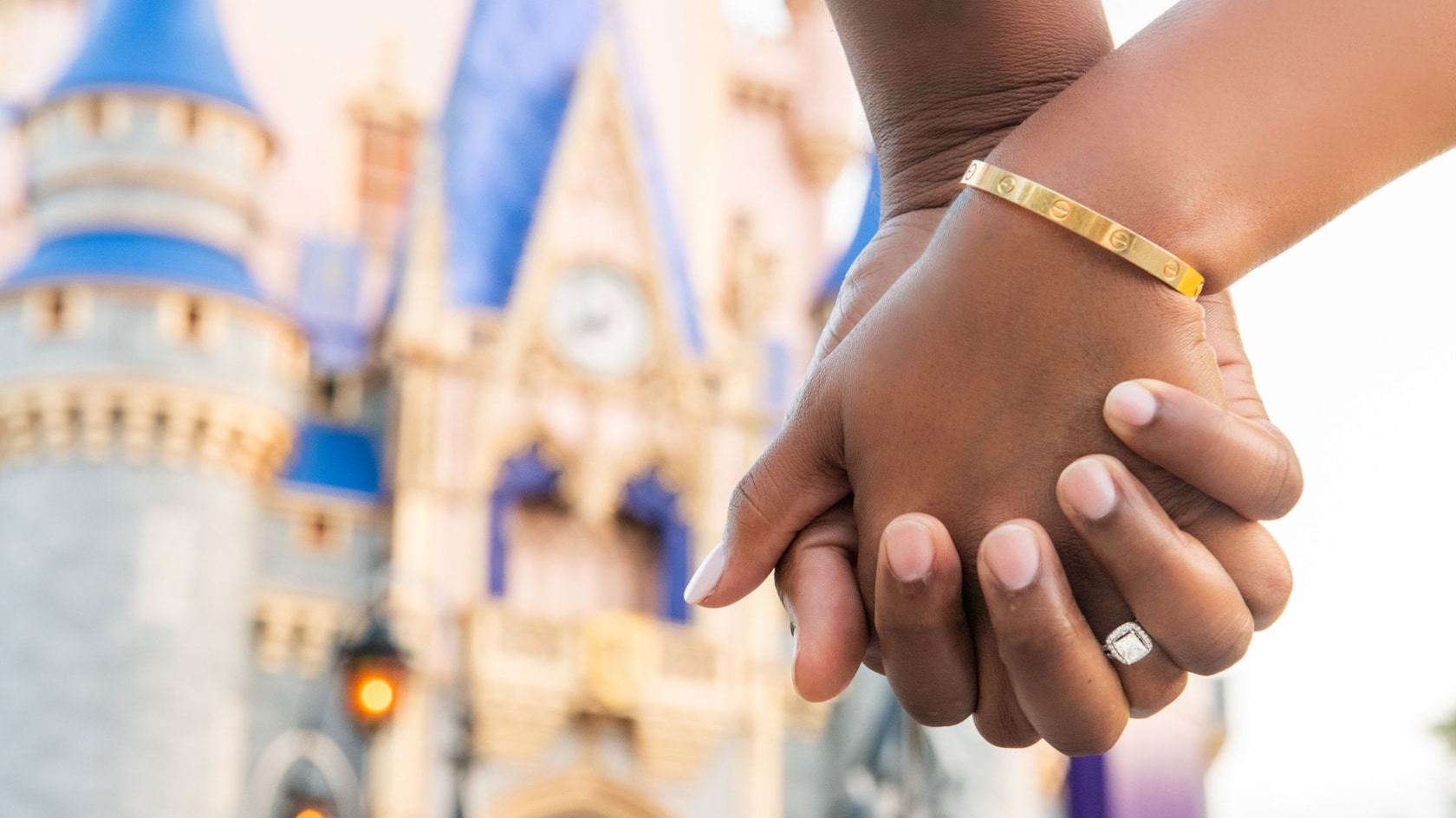 Two hands tightly clasped, with Cinderella Castle in the background
