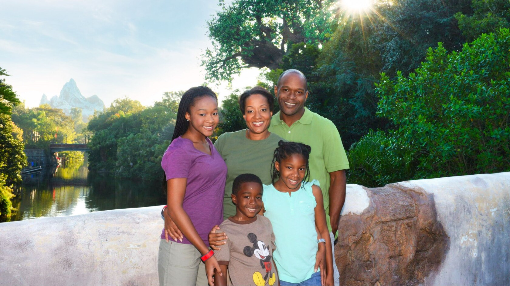 An African American father and mother pose with their three smiling children in Disney’s Animal Kingdom park, with the iconic Tree of Life in the background