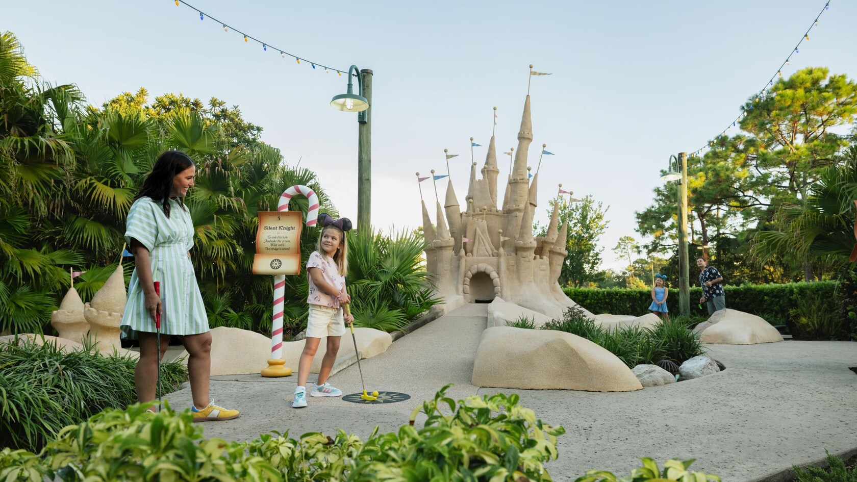 A mother and daughter playing miniature golf on a beach themed course at Winter Summerland Miniature Golf featuring a large sandcastle structure