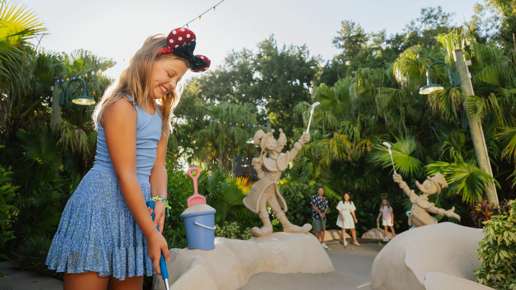A child playing miniature golf with her family at Winter Summerland Miniature Golf featuring sandcastle structures shaped like Goofy and Donald Duck