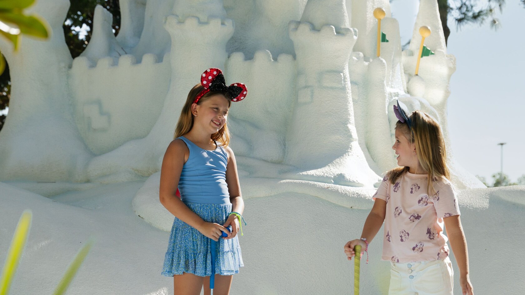 Two children holding putters while standing in front of large white sandcastle structure at Winter Summerland Miniature Golf