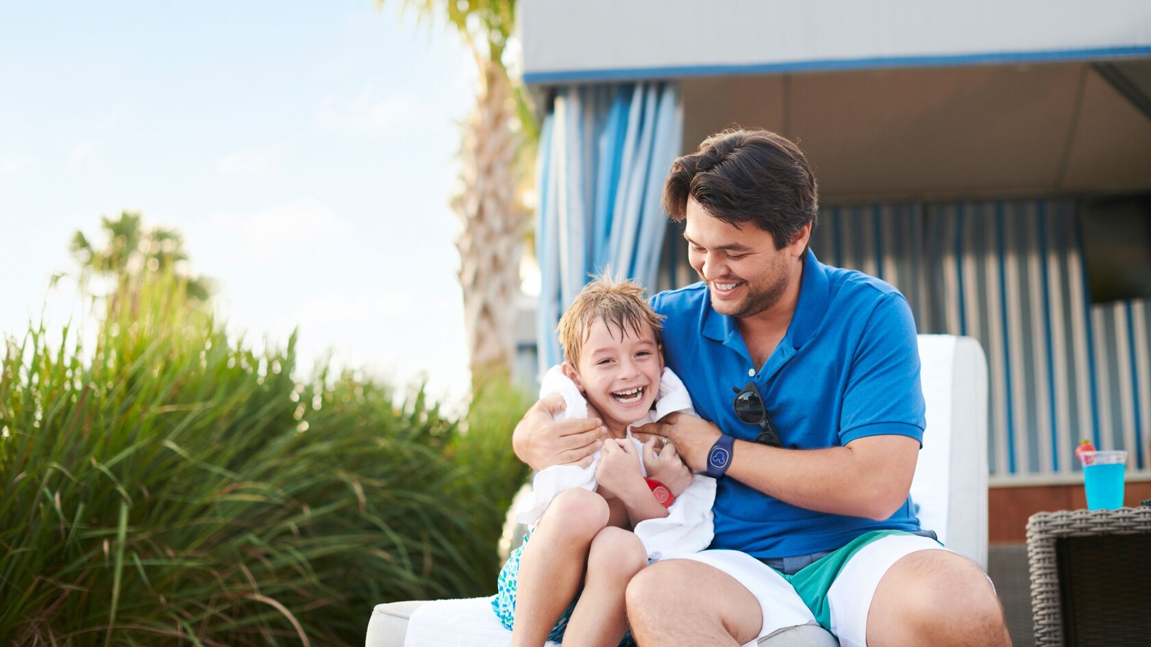 A father wrapping his smiling son in a towel as they sit on a lounge chair at a Disney Resort hotel