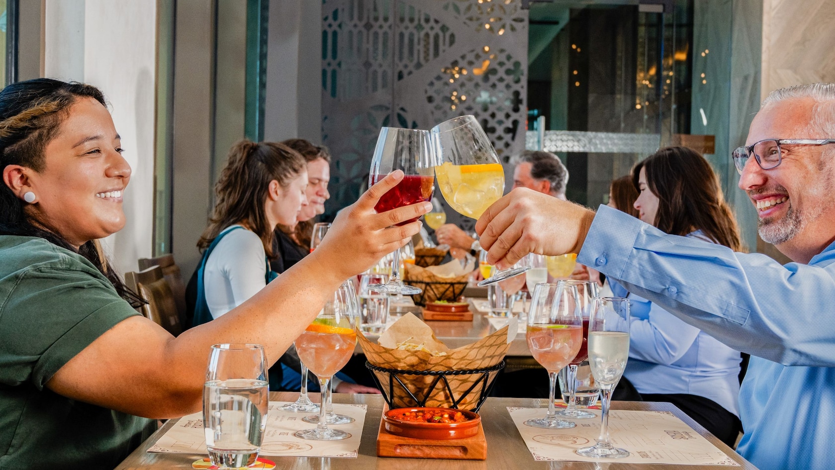 A smiling couple clinking their glasses across a table before taking a sip from their beverages