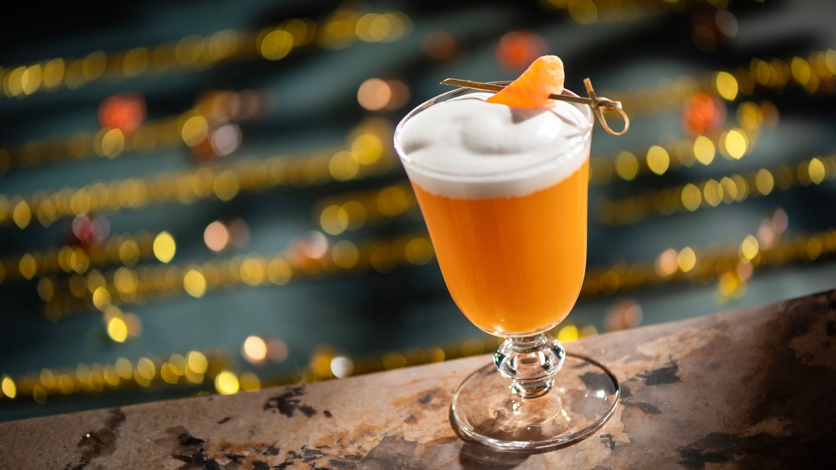 A frozen orange cocktail topped with foam and a dried citrus garnish from Hurly Burly at Disney’s Boardwalk