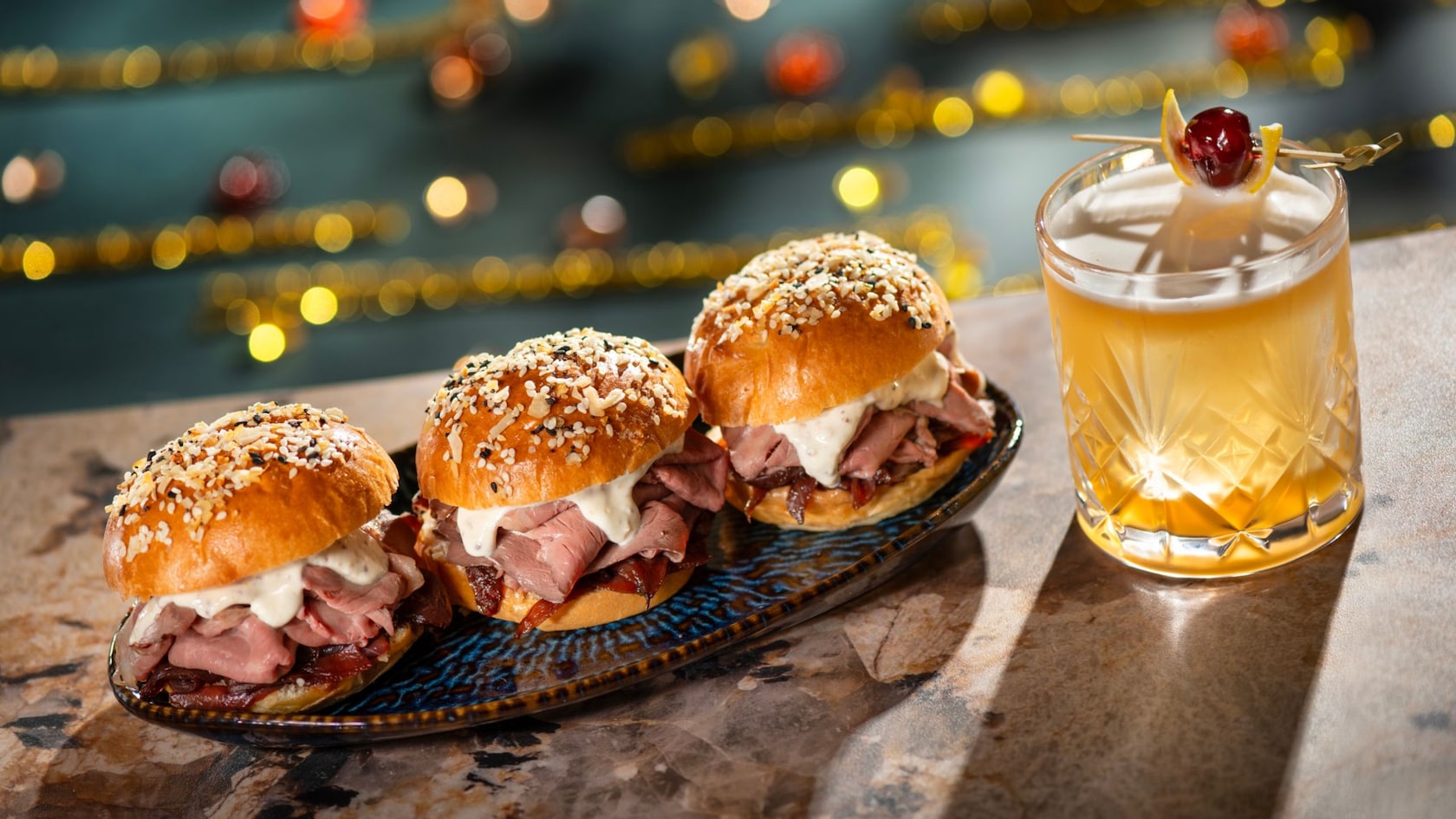 Three roast beef sliders on seeded buns beside an amaretto sour cocktail from Hurly Burly at Disney’s Boardwalk