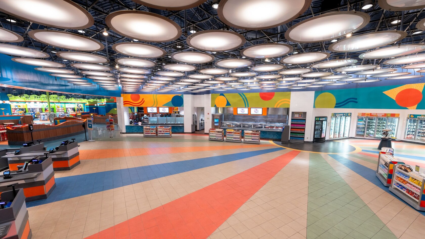 A food court with service stations, shelves of snacks, refrigerated cabinets and checkout counters at Everything Pop Shopping & Dining in Disney’s Pop Century Resort