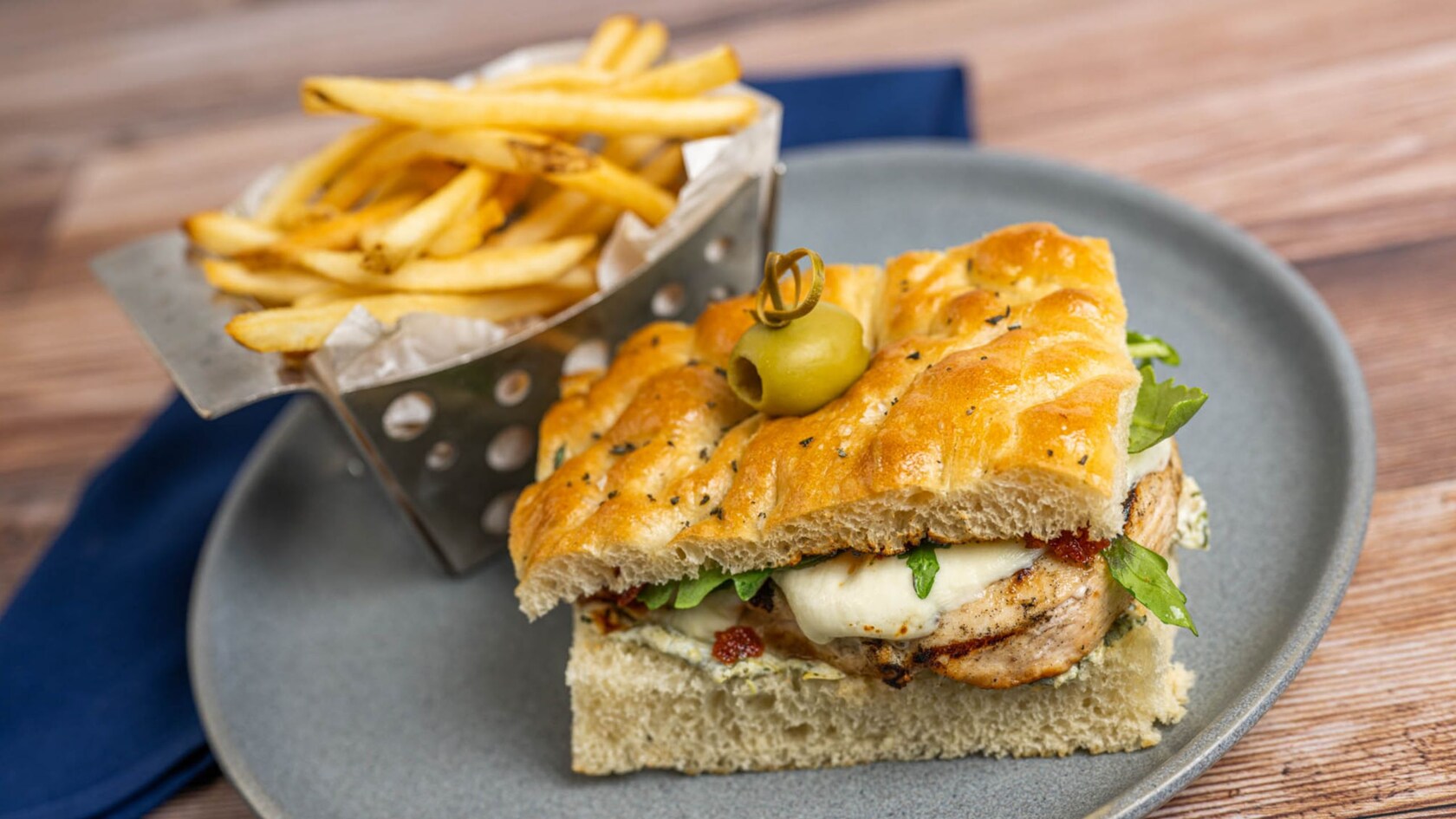 A grilled chicken sandwich with a basket of French fries on a plate from Primo Piatto