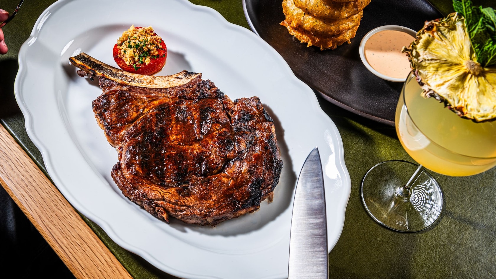 Un bistec Tomahawk, una torre de onion rings y un cóctel en Bourbon Steak