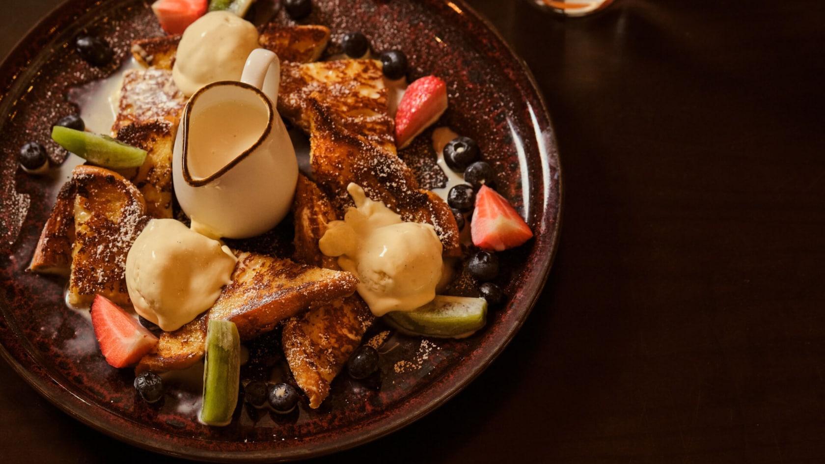 French toast topped with scoops of vanilla ice cream, blueberries, strawberries and kiwi