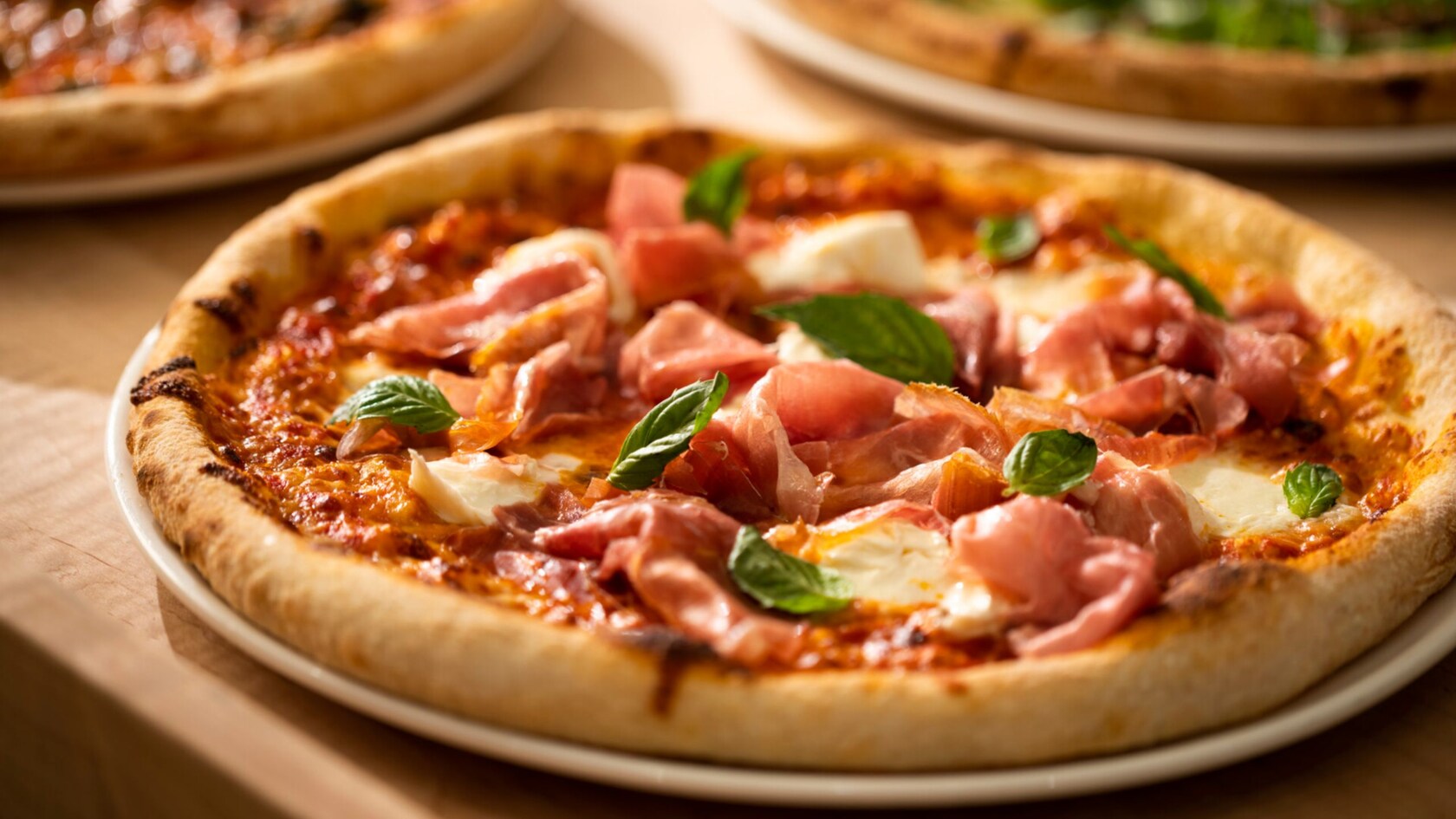 Three pizzas including one with prosciutto, fresh mozzarella and basil