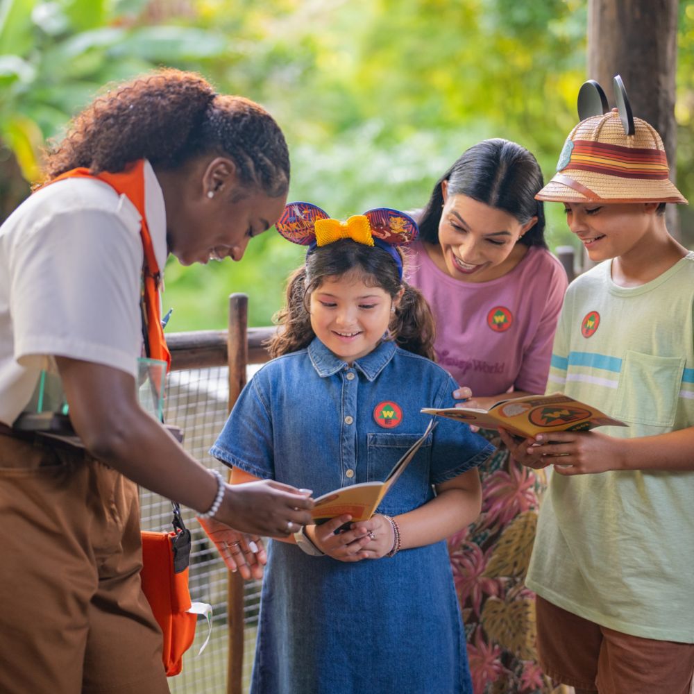 A family of 4 reading a Wilderness Explorer handbook along with a Cast Member in Disney's Animal Kingdom theme park