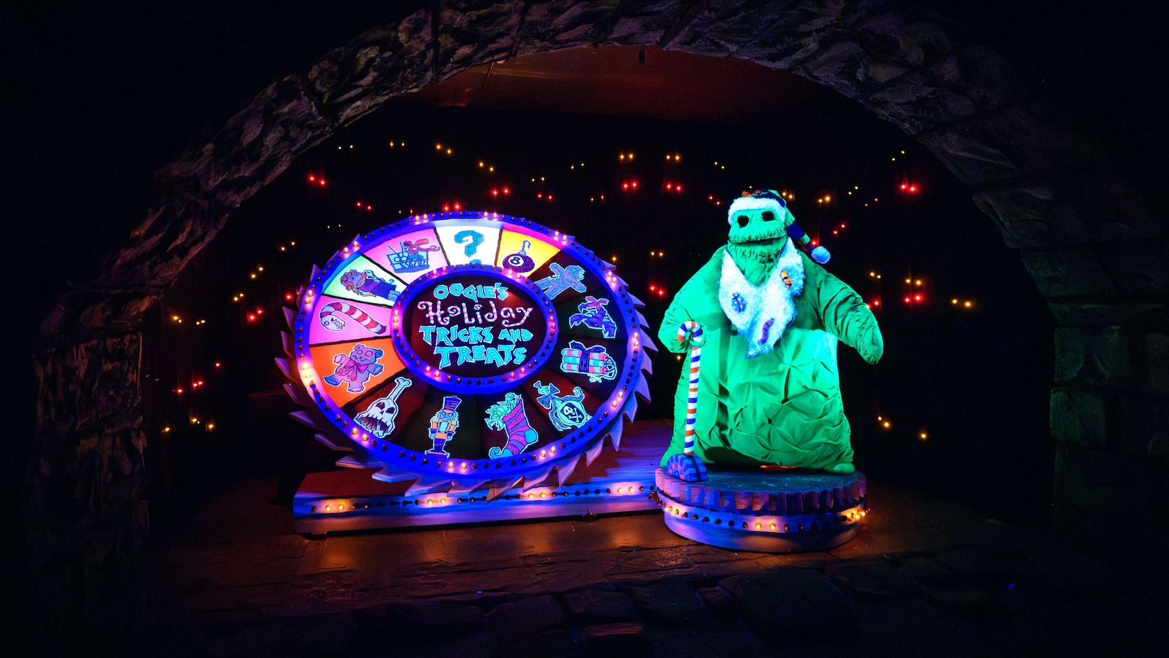 Oogie Boogie standing next to Oogie’s Holiday Tricks and Treats wheel at Haunted Mansion Holiday