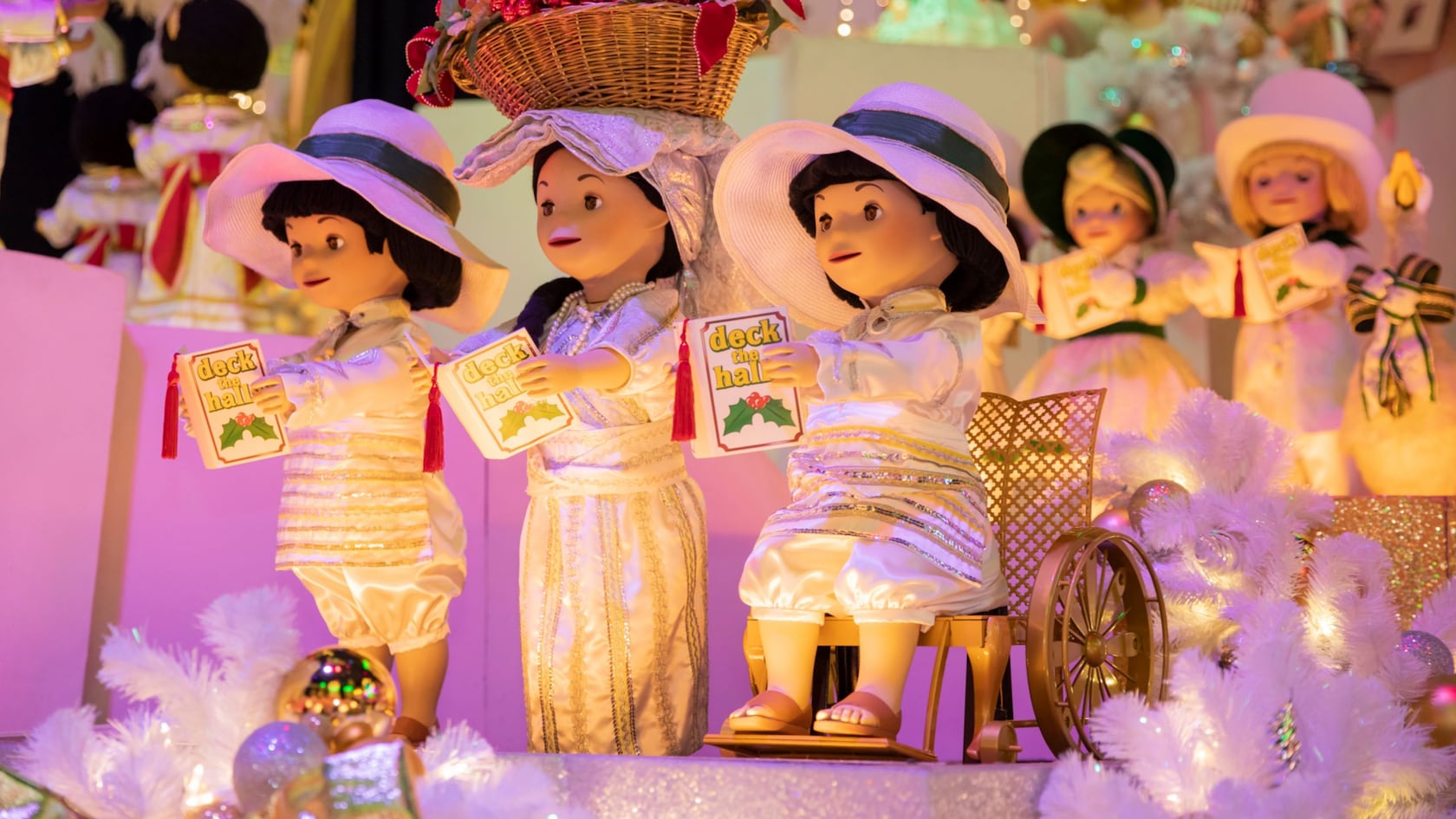 3 animatronic dolls hold books that read ‘deck the halls’ on ‘it’s a small world’ in Magic Kingdom park