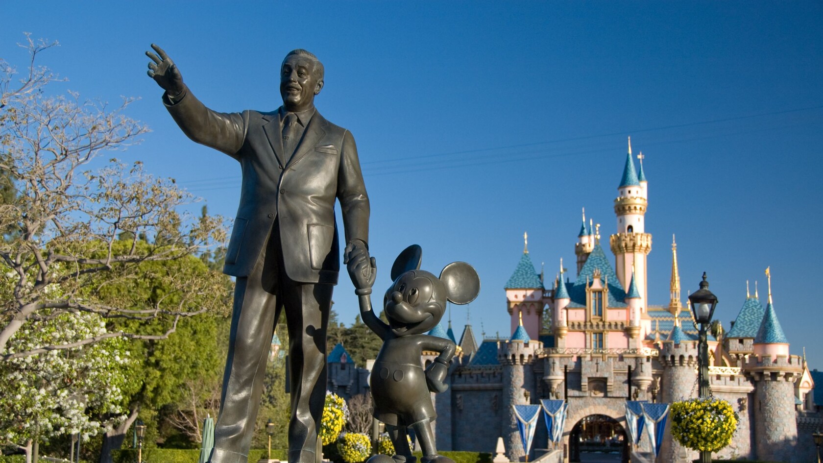 A statue of Walt Disney and Mickey Mouse in front of Sleeping Beauty Castle in Disneyland Park