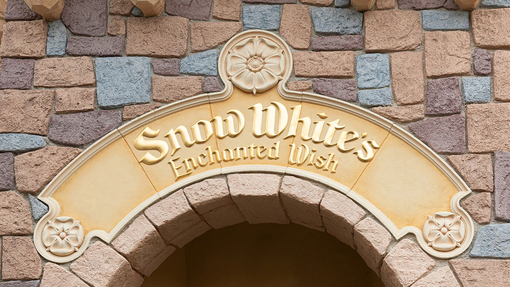 An entrance sign that reads ‘Snow White’s Enchanted Wish’ above an archway at Disneyland Park in California