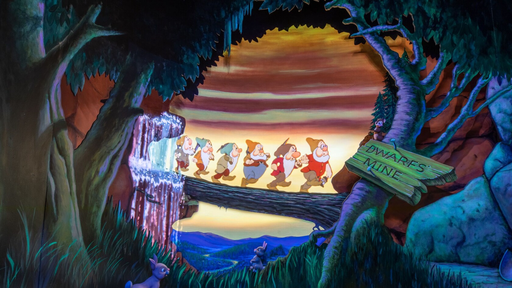 An illustration showing 6 of the 7 Dwarfs crossing a log bridge in a forest as they head to the Dwarfs mine