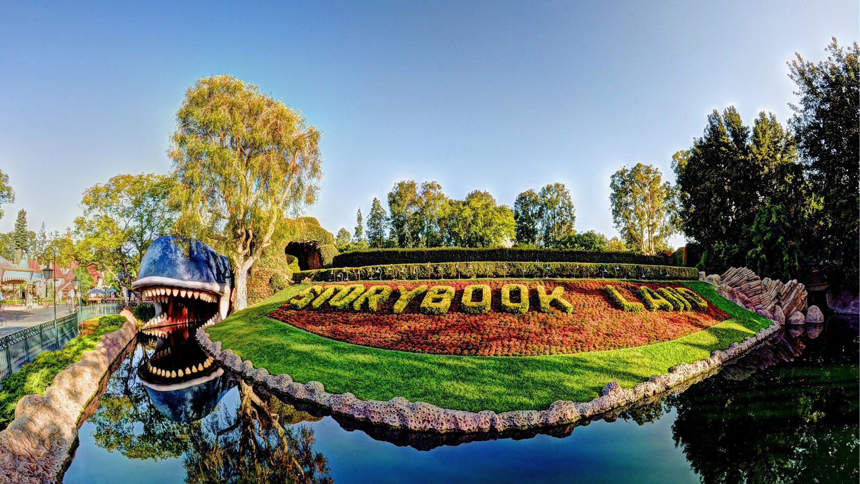 Un jardín de poda ornamental con arbustos que forman el nombre de Storybook Land en medio del canal de la atracción