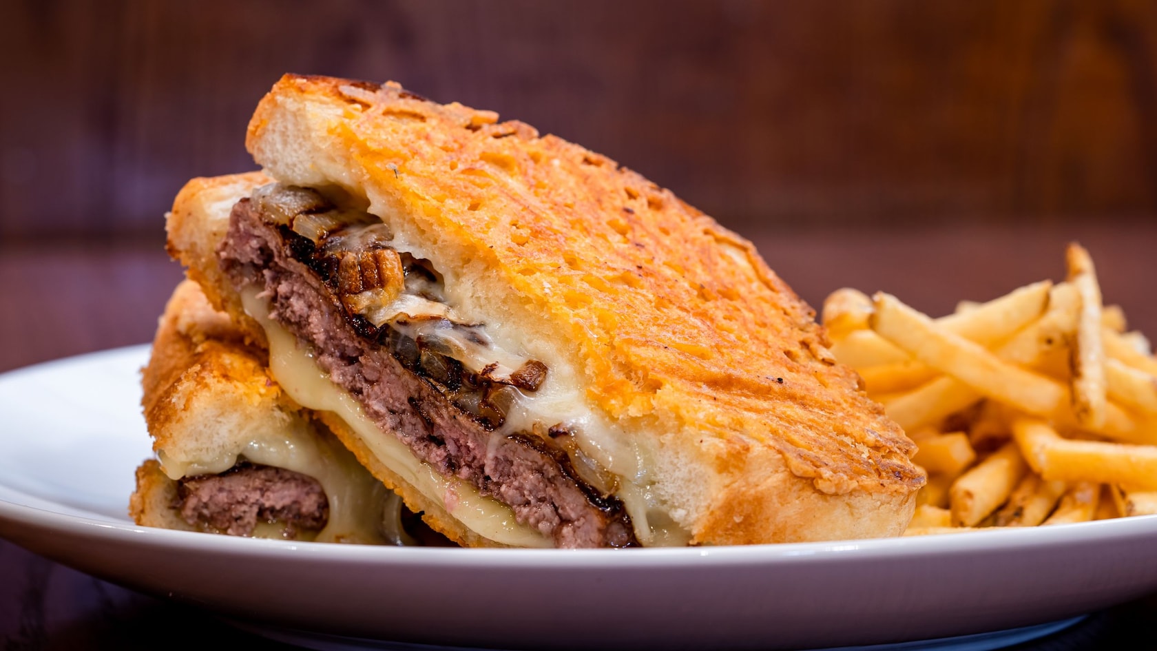 A Parmesan Toasted Patty Melt with cheese and grilled onions plated next to a pile of French fries