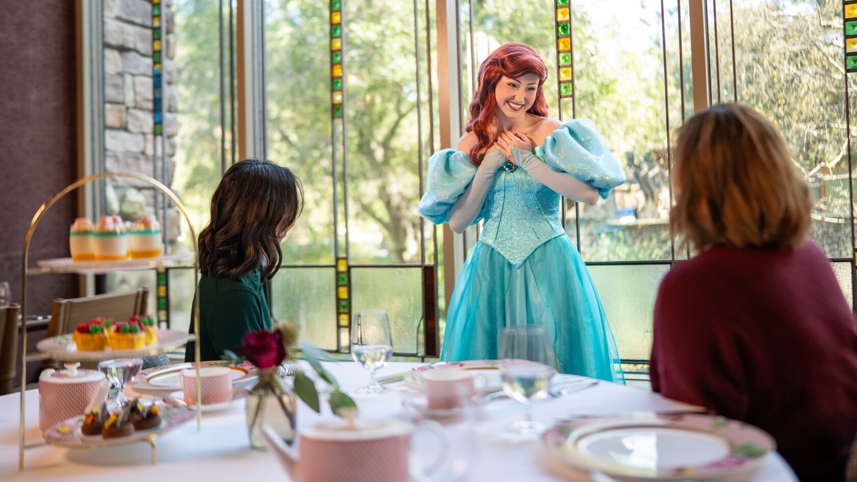 Two Guests sitting at a table while greeting Princess Ariel during Disney Princess Breakfast Adventures