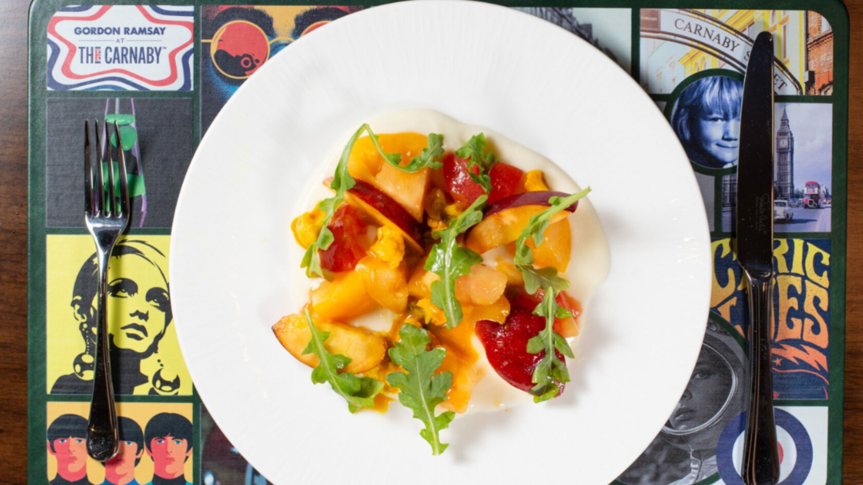 A burrata salad featuring burrata topped with heirloom tomatoes, stone fruit, arugula leaves and dressing
