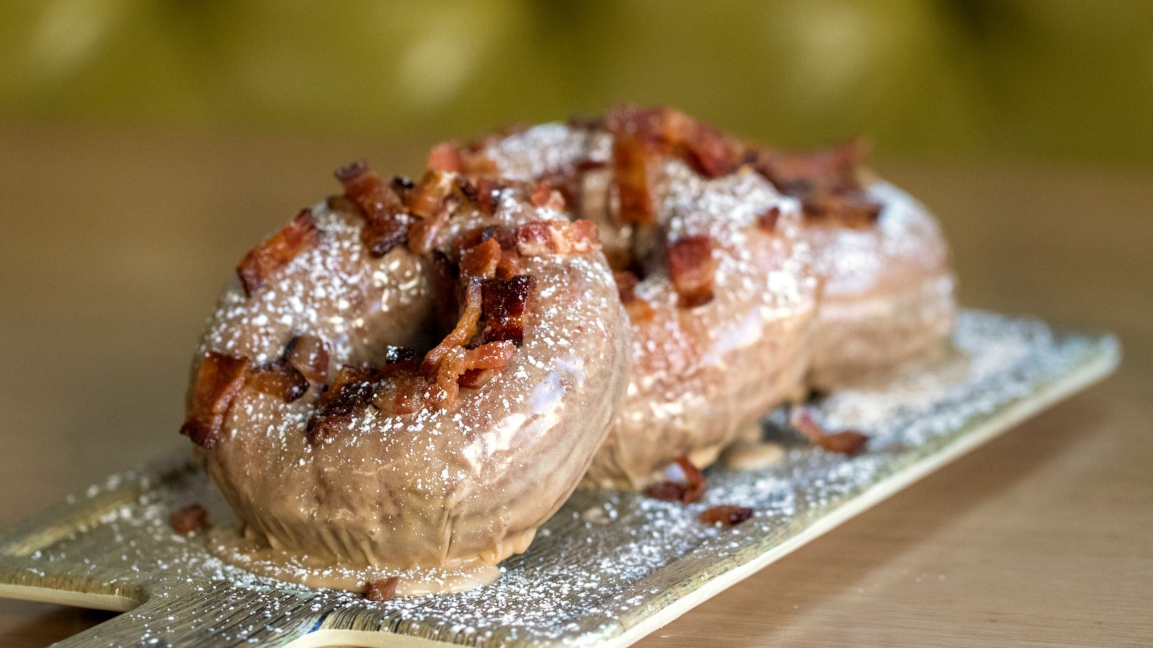 A plate with three donuts topped with bacon pieces