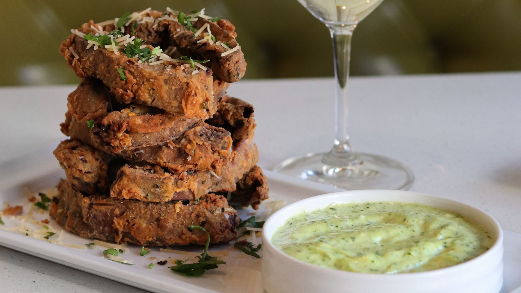 A plate of fried portebello mushrooms with a green sauce