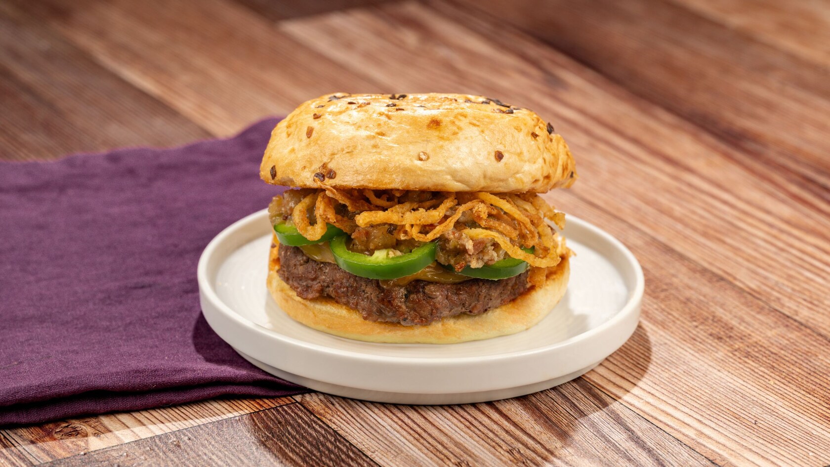 A beef burger with jalapeno cheese sauce, crispy onions and other ingredients on an onion roll
