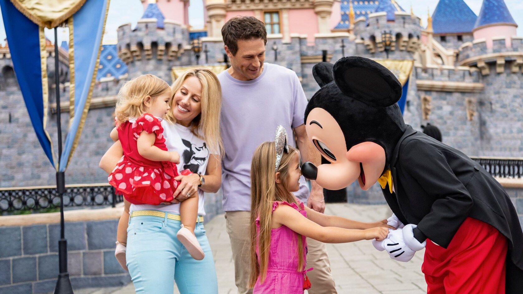 Mickey saluda y toma de la mano a una niña con su familia, frente al Castillo de la Bella Durmiente.