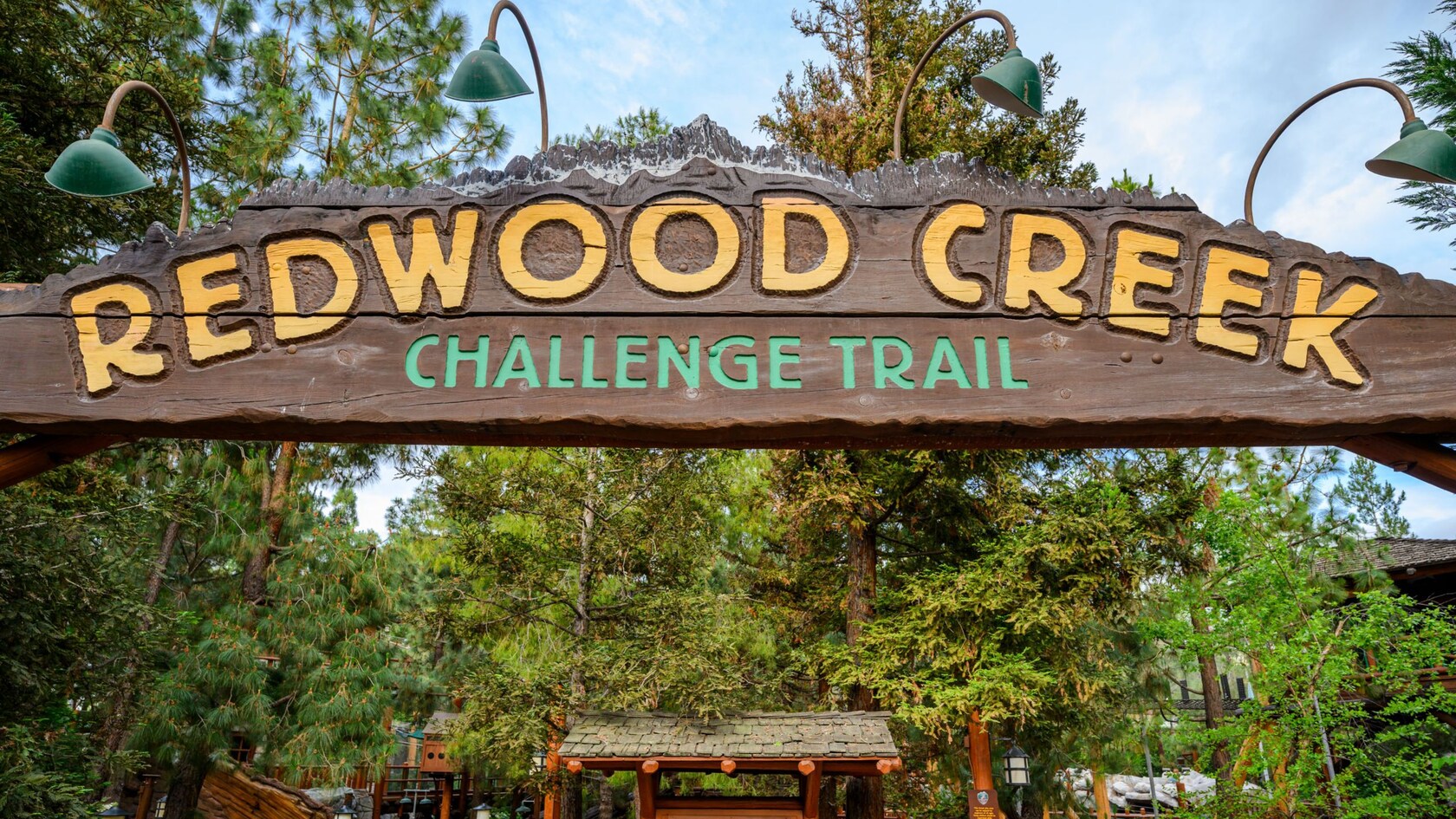 A large wooden sign that reads ‘Redwood Creek Challenge Trail”, with redwoods and pine trees behind it