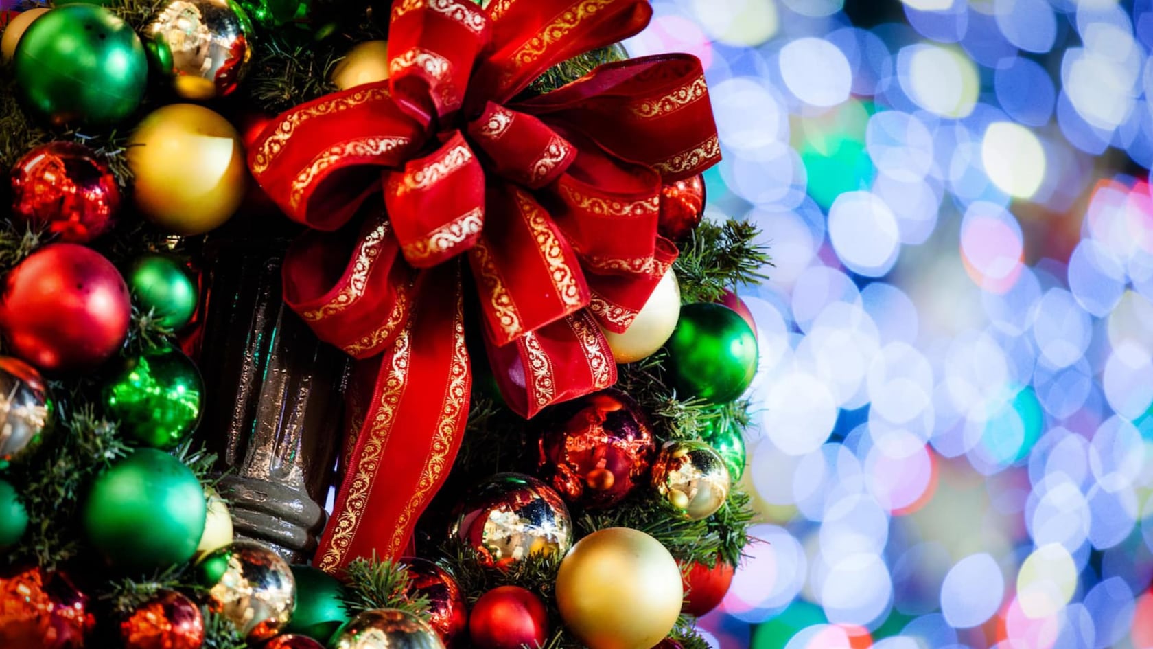 A large bow attached to a lamppost surrounded by a wreath of Christmas ornaments