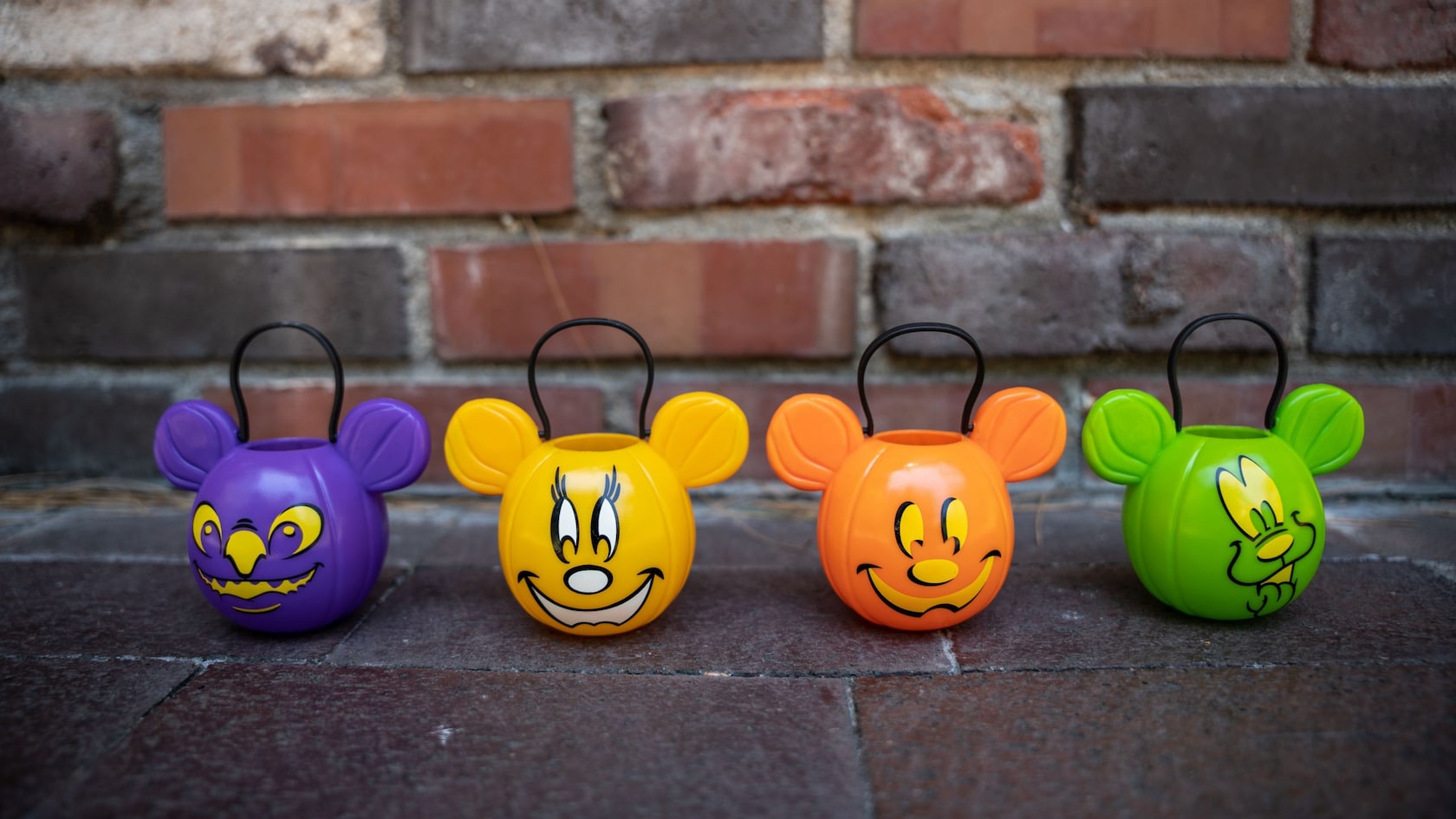 Four plastic pumpkins, each featuring Mickey ears and a handle, decorated with different faces