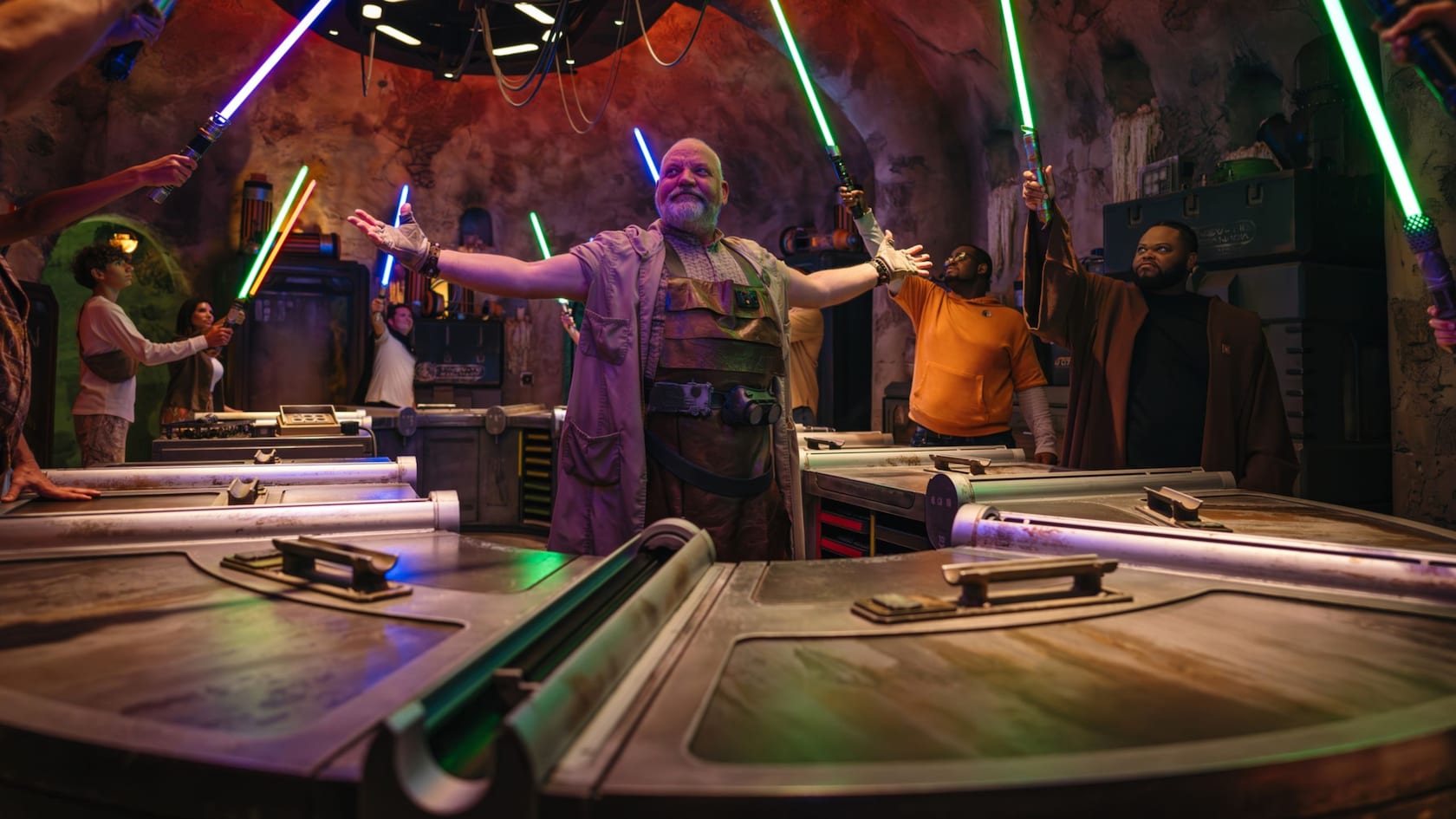 A character stands with arms outstretched as Guests raise their glowing lightsabers