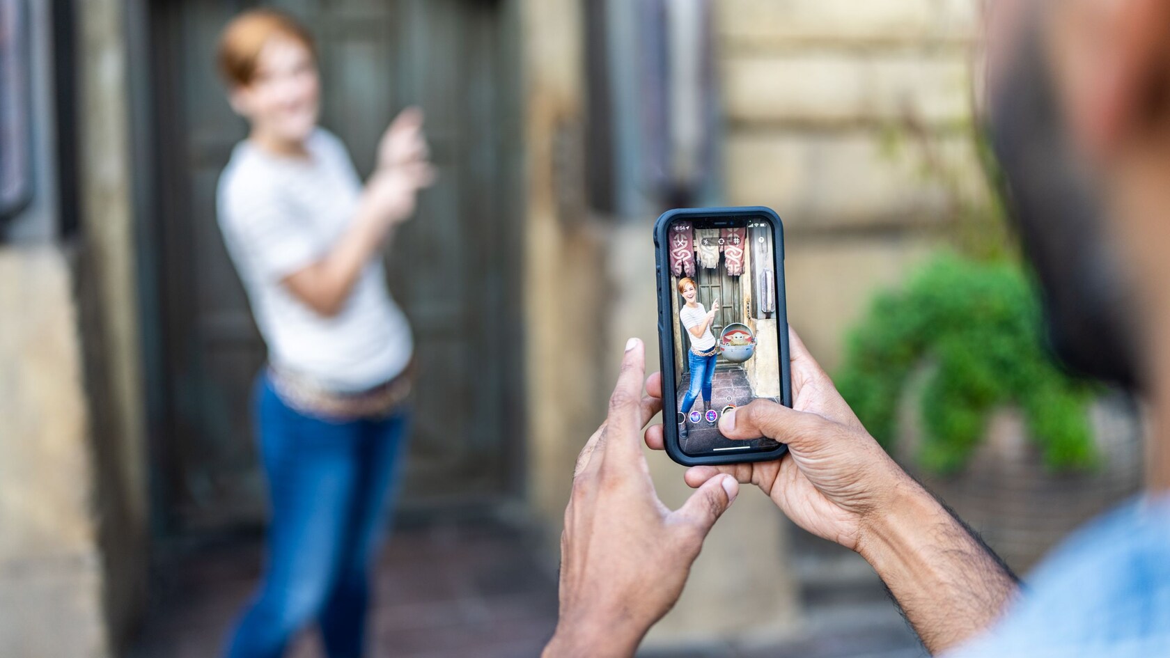 A Guest poses solo for a picture, but on the mobile device capturing the image, Grogu hovers in a pod next to the Guest