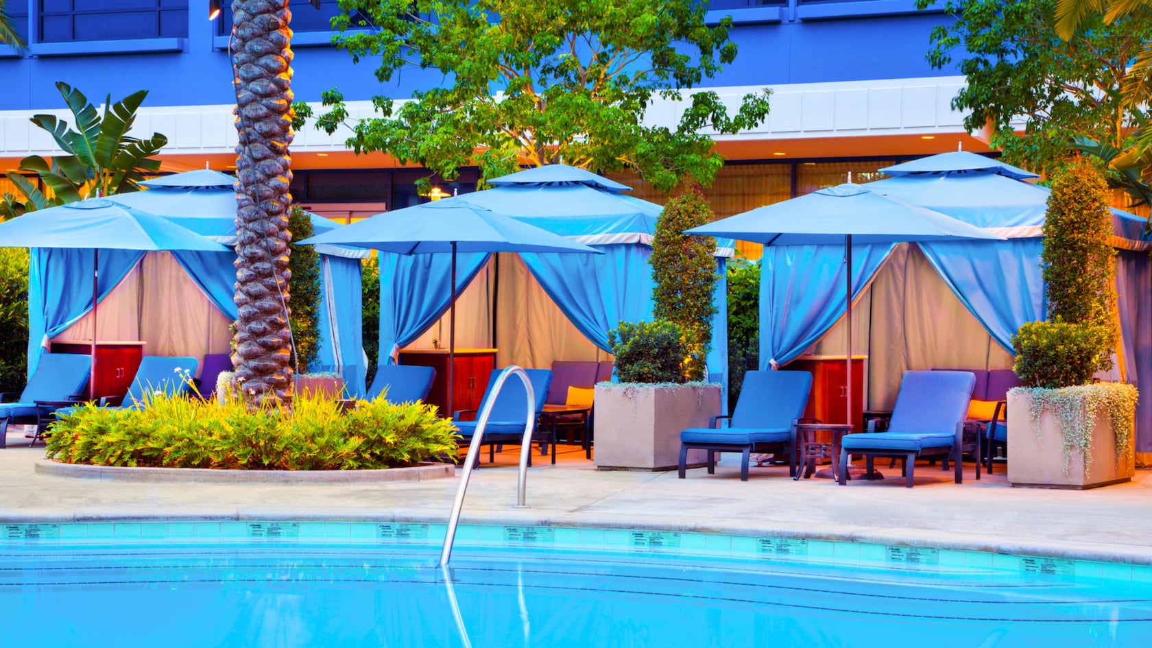 Three poolside cabanas with sofas, tables, chaise lounge chairs and umbrellas