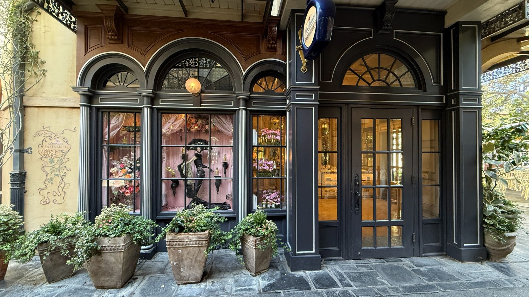 The façade of Mademoiselle Antoinette's Parfumerie with large windows displaying fragrance bottles, floral arrangements and a mannequin